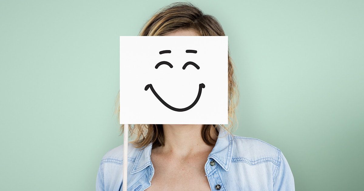 A mosoly mögött gyakran több rejlik, mint amit látunk Egy nő maga elé tart egy mosoly táblát, de valójában mögötte szomorú és lelki problémákkal küzd, de kifele azt tükrözi, hogy boldog és minden rendben.