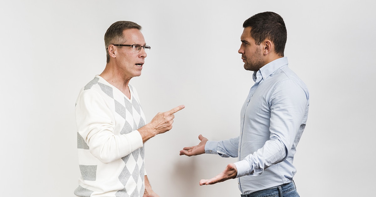 Asszertivitás és dominancia, avagy határozottság vagy hatalmaskodás. Hol válik el a kettő fogalom? Két férfi vitázik, egyik nyugodt és kérdez, a másik erőszakos testtartásban le akarja győzni a szavaival